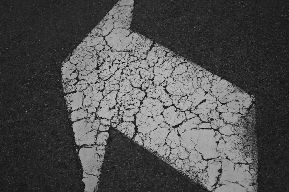 Ein weißer, rissiger Richtungspfeil auf dunklem Asphalt